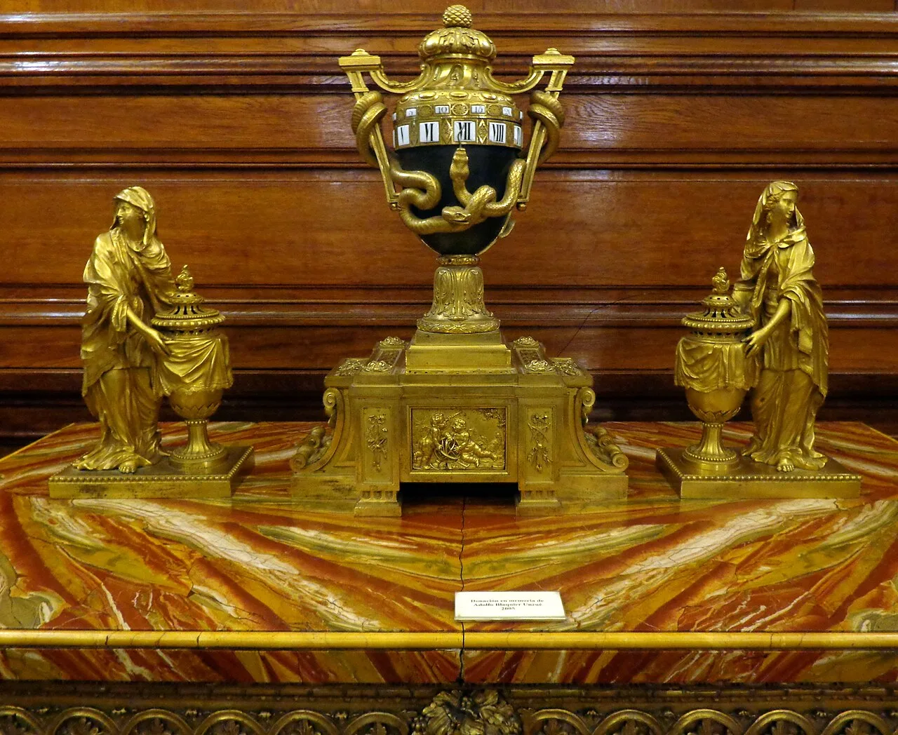 ساعة من البرونز المنقوش والمذهّب من عهد لويس السادس عشر، صُنعت في فرنسا عام 1768، بين مبخرتين من الطراز نفسه